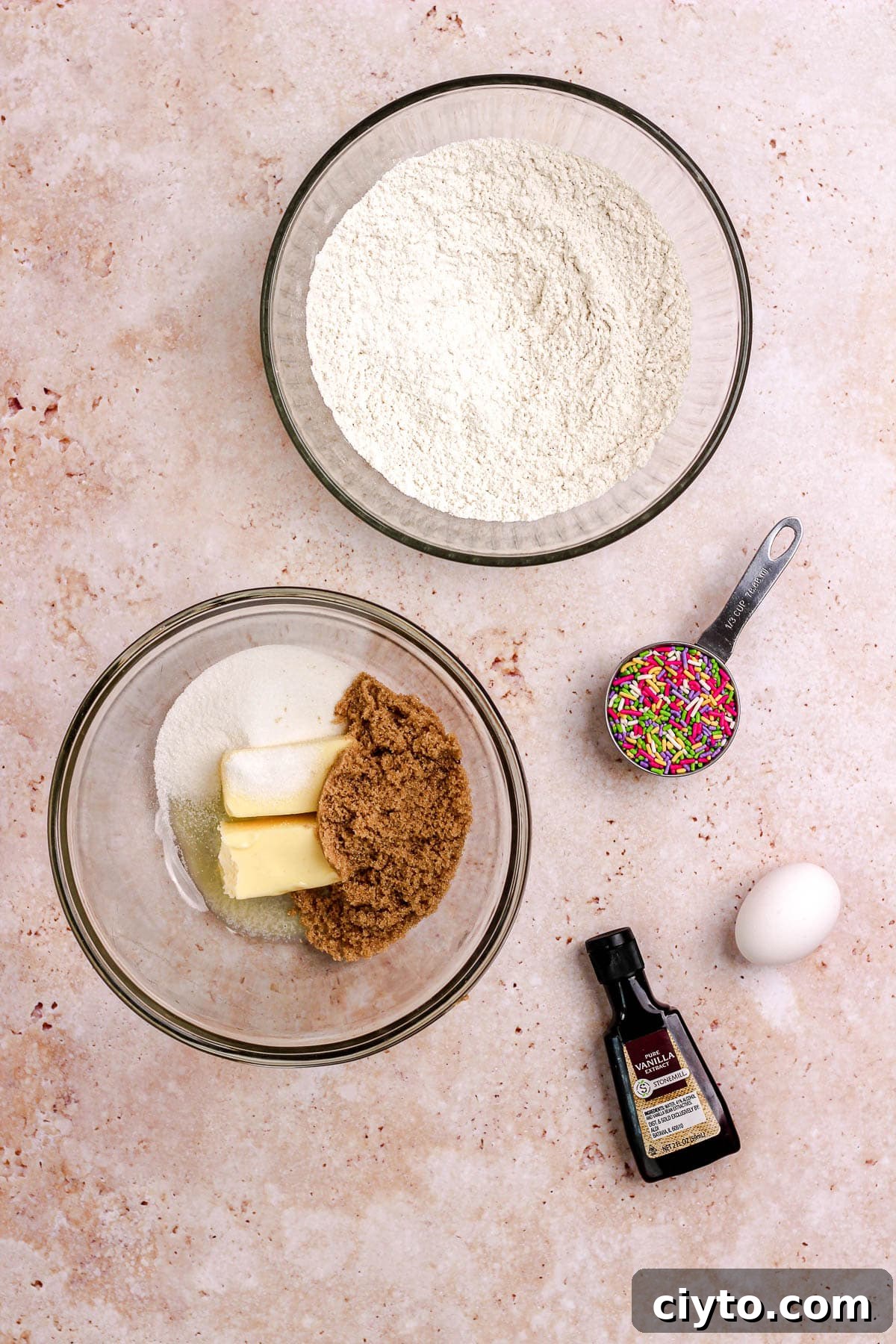 An ingredient shot of ingredients for sprinkle sugar cookies on a pink backdrop.