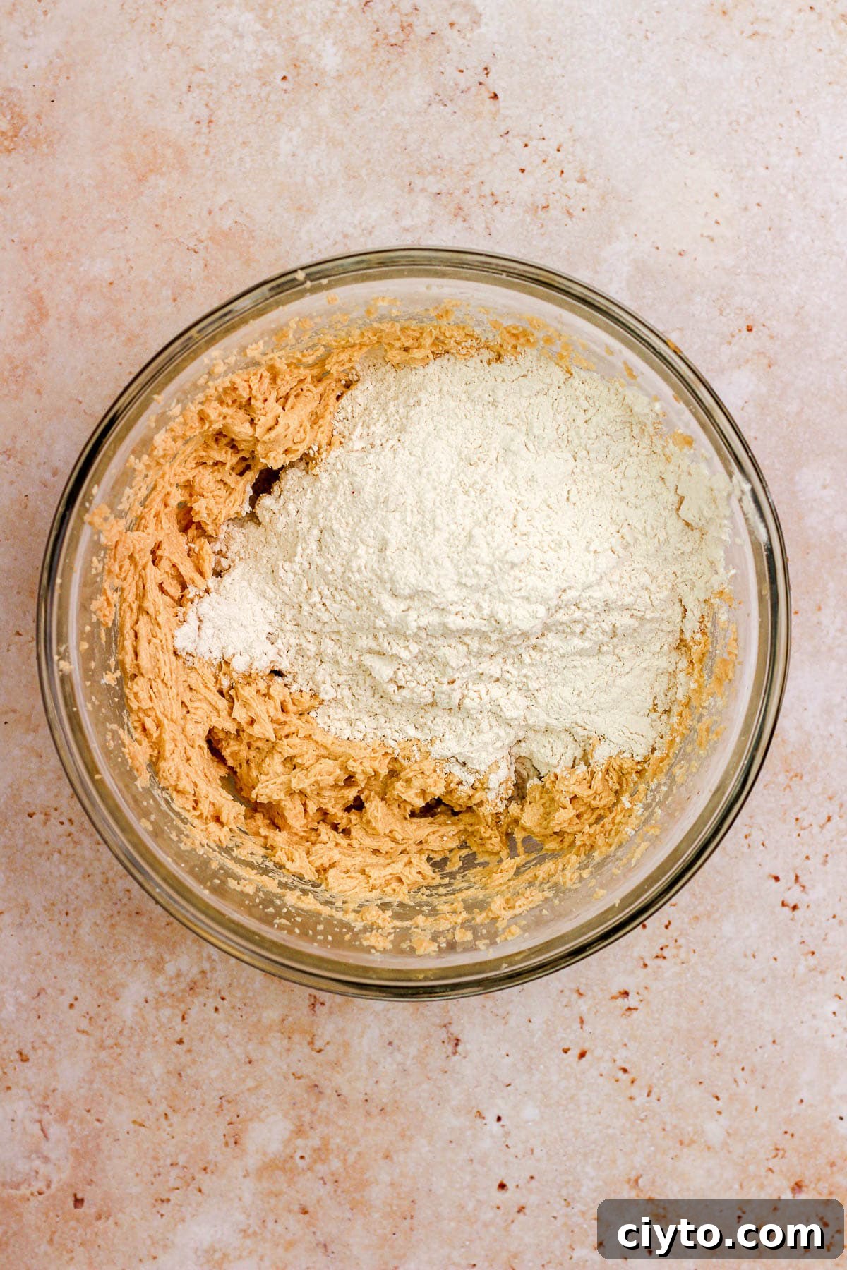 A glass bowl filled with sugar cookie dough and flour.