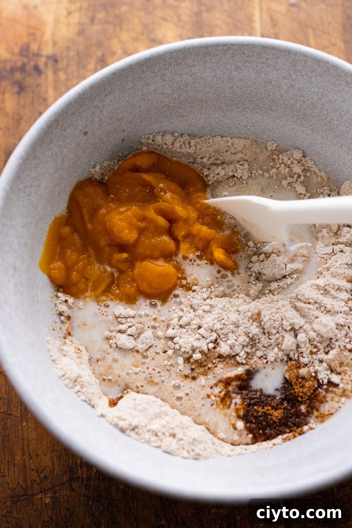 Ingredients for pumpkin pancakes being stirred in a white bowl with a rubber spatula.