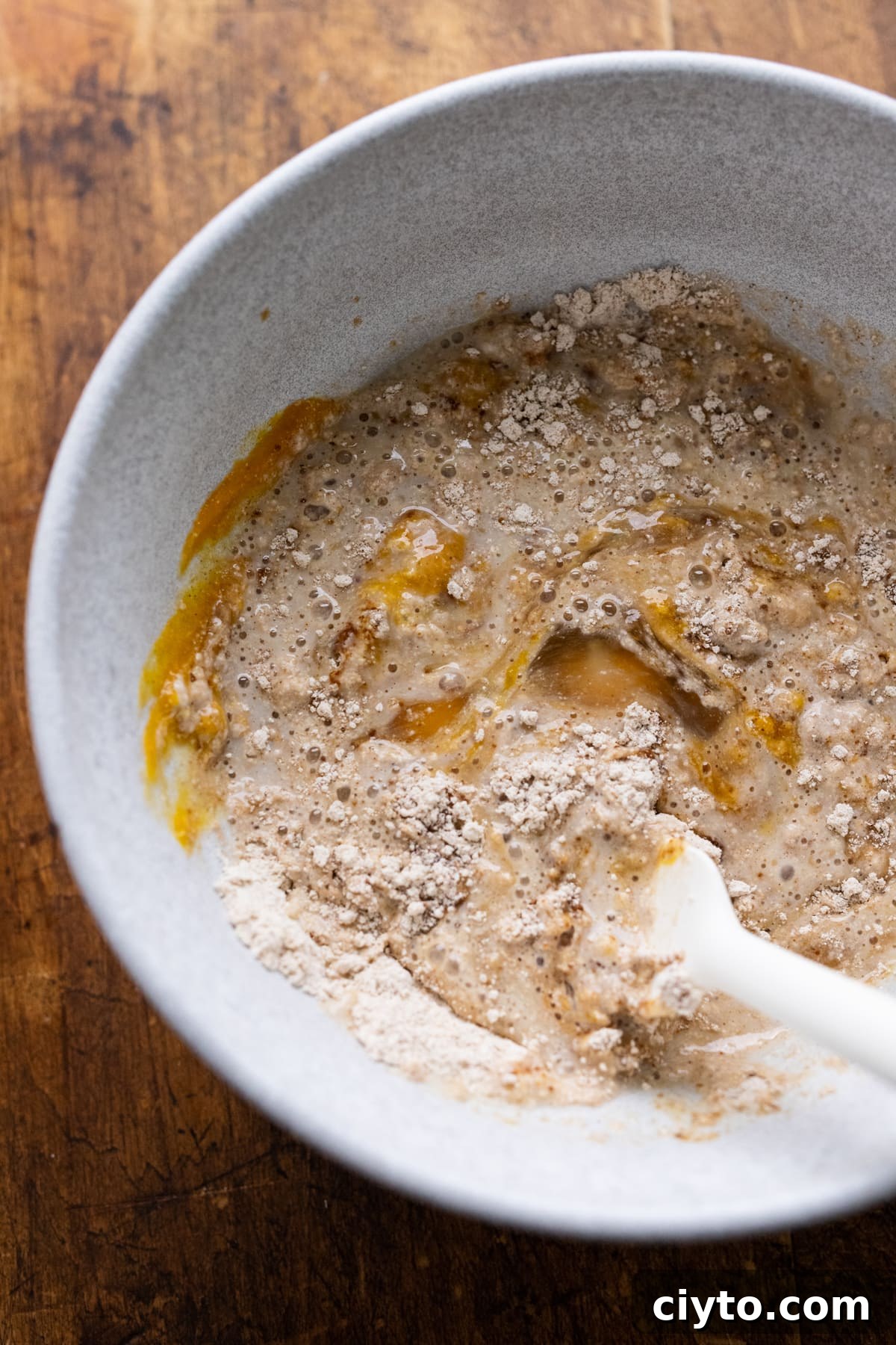Pumpkin pancake batter being stirred with a white rubber spatula in a white bowl.