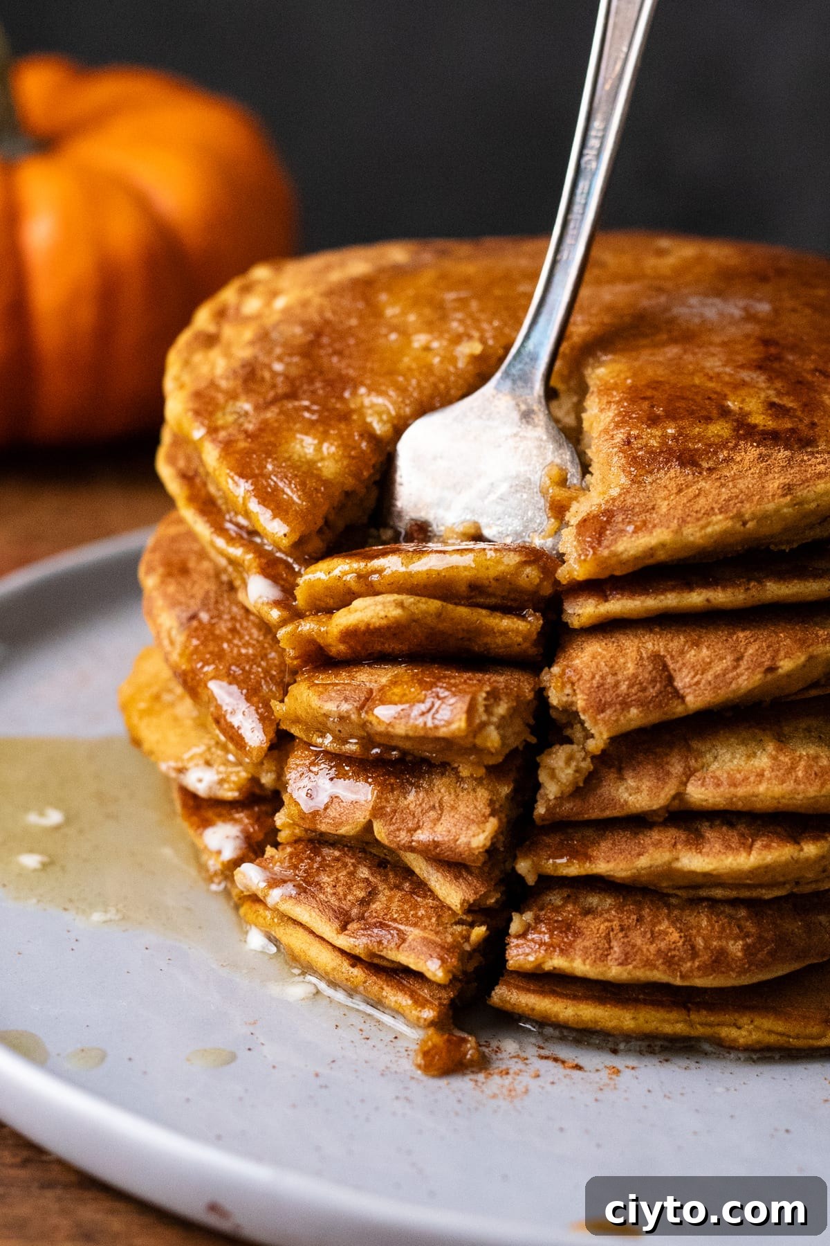 A close up of a stack of pumpkin spice pancakes with a fork in it.