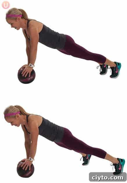 Chris Freytag demonstrating a plank jack using a medicine ball wearing a black top and exercise pants.
