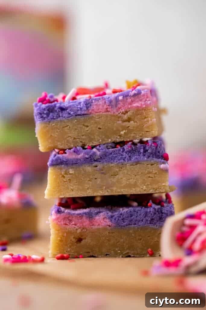 Valentine’s Day sugar cookie bars stacked with pink and purple frosting and festive sprinkles