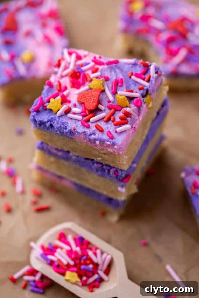 Stacked Valentine’s Day sugar cookie bars with pink and purple frosting and sprinkles