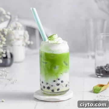 green milk tea in a glass cup with frothed milk and dusted with matcha powder.