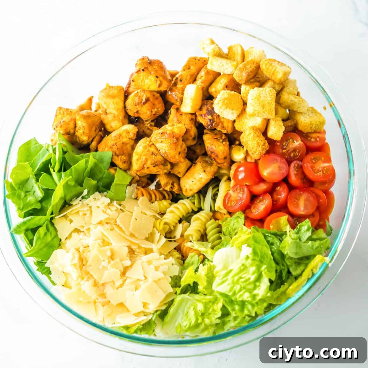 Chicken Caesar Pasta Salad Recipe with Crispy Croutons 6 Lettuce, pasta, chicken, croutons, parmesan, and tomatoes combined in large bowl.
