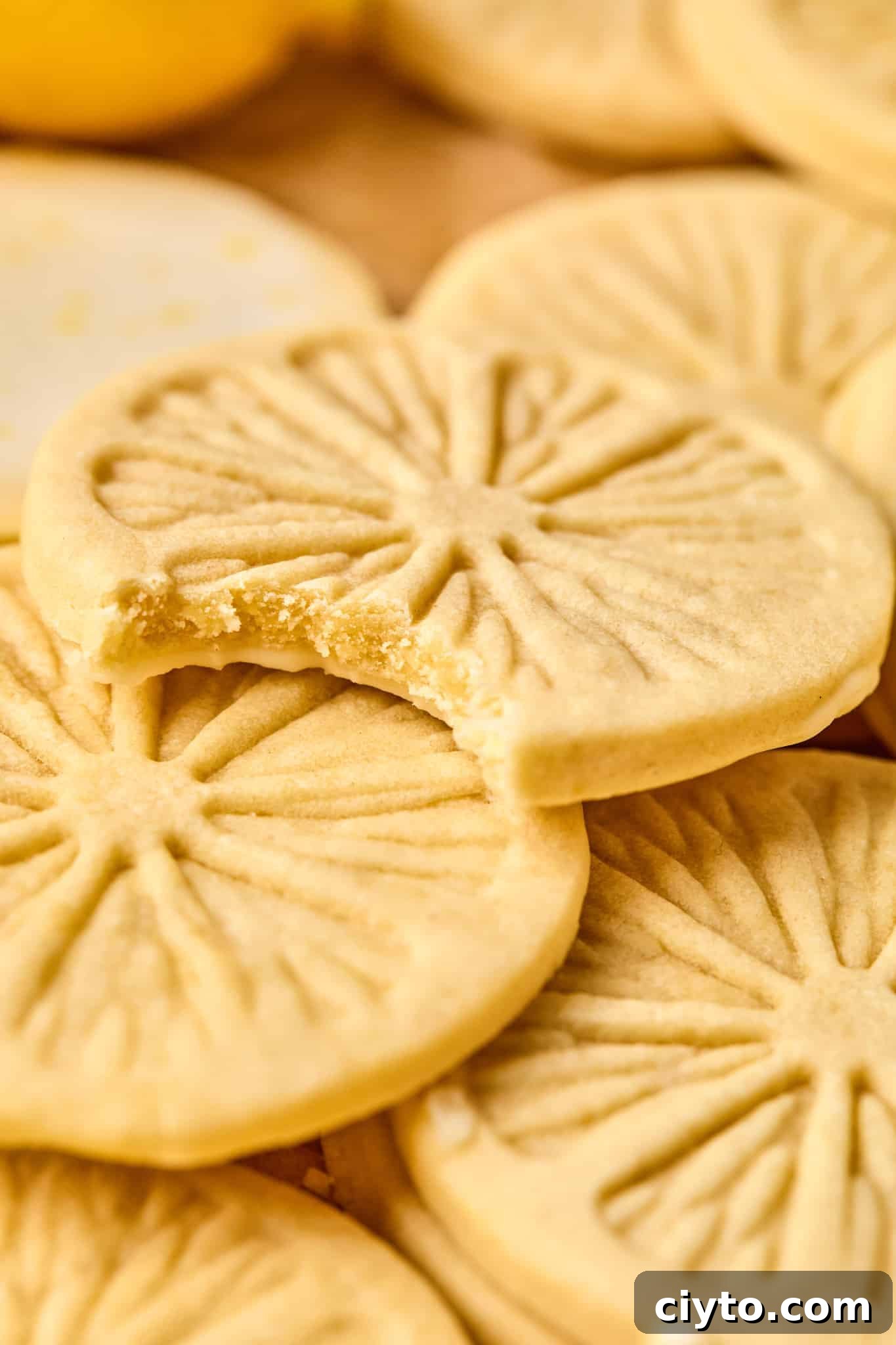 Lemonade cookies piled on top of each other and the top cookie has a bite taken out of it showing the inside of the cookie.