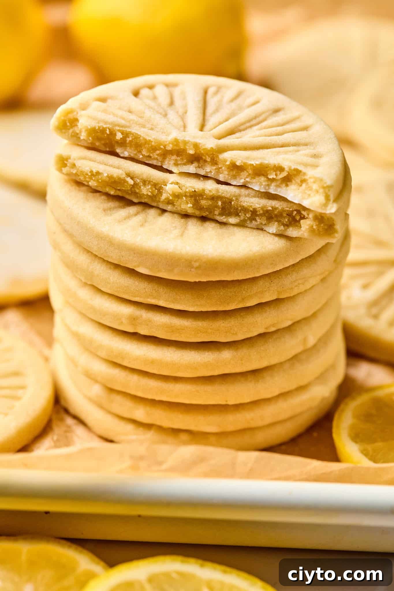 Stack of copycat girl scout lemonade cookies on parchment-lined baking sheet. The top two cookies are cut in half so you can see the middle of the cookie.