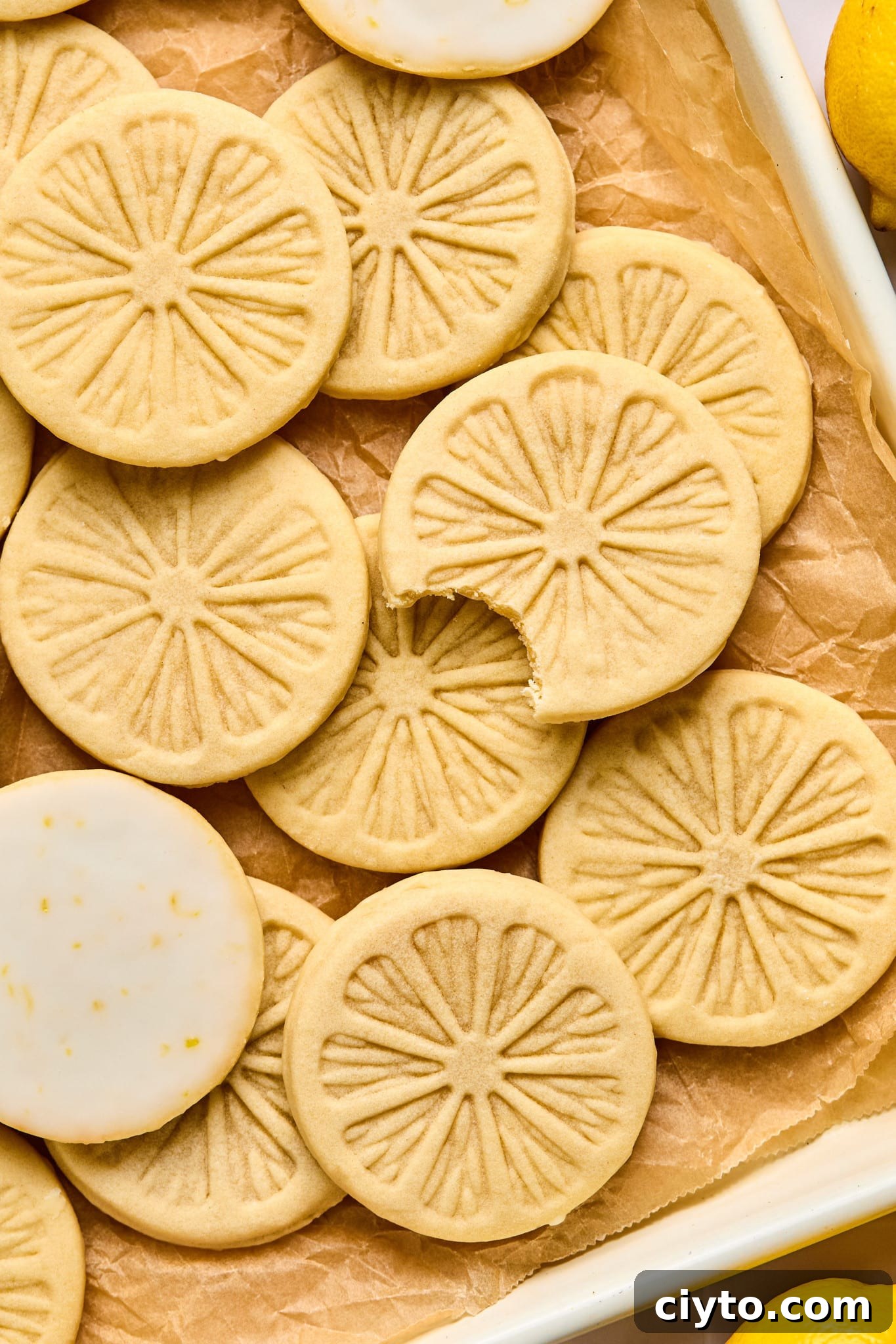 Lemonade cookies on parchment-lined baking sheet after they have finished setting from being dunked in the glaze. One cookie has a bite taken out of it and two of the cookies are showing the lemon glaze on the bottom.