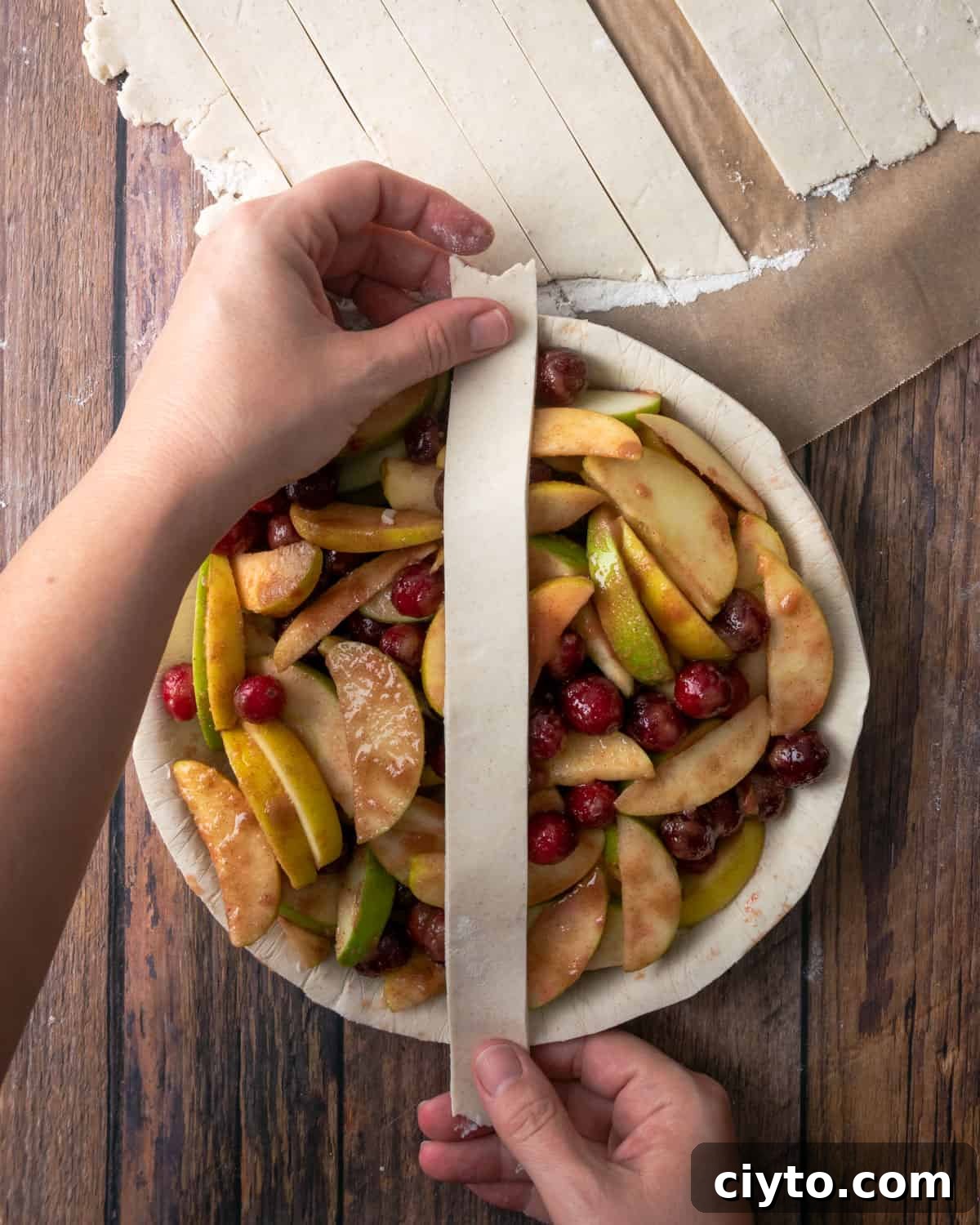 How to Make a Flaky Gluten-Free Pie Crust 22 A strip of pie dough being placed over the top of an unbaked apple cranberry pie.
