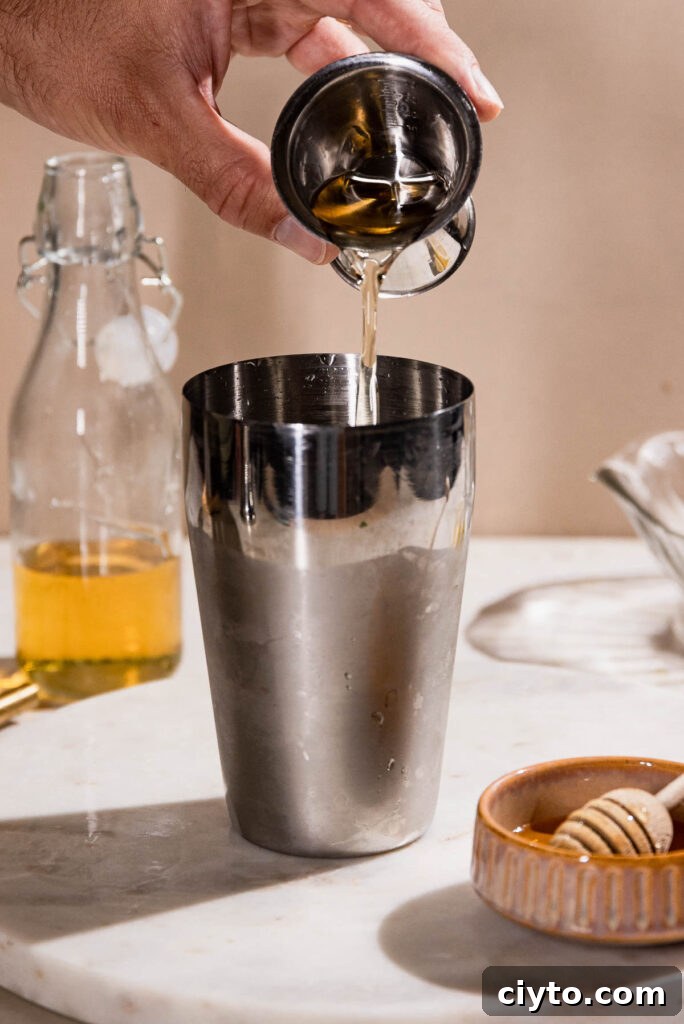 Classic Bee's Knees Cocktail Recipe 5 Honey syrup being poured into a cocktail shaker.