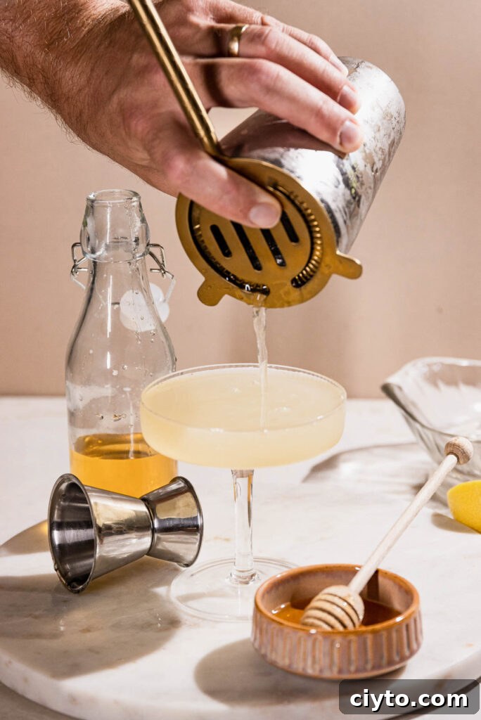 Classic Bee's Knees Cocktail Recipe 8 Cocktail being strained into coupe glass.