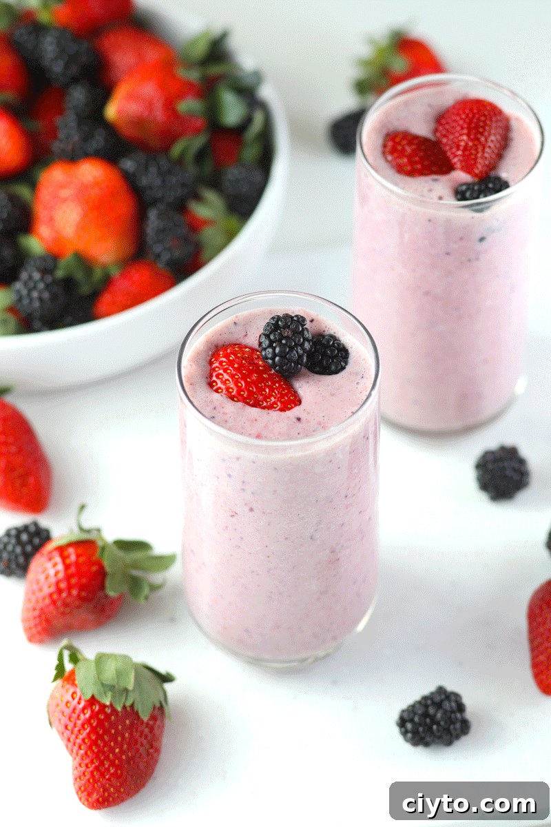 A fruit and yogurt smoothie with fresh strawberries and blackberries around them.