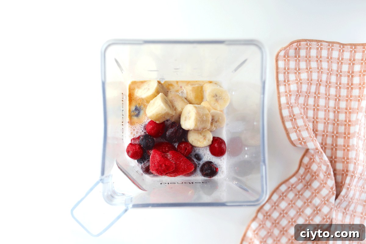 A blender with smoothie ingredients in it. Frozen berries, frozen bananas, milk and vanilla.