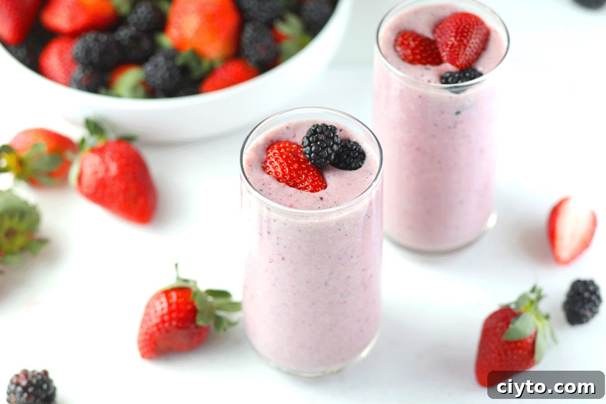 A fruit and yogurt smoothie with fresh strawberries and blackberries around them.