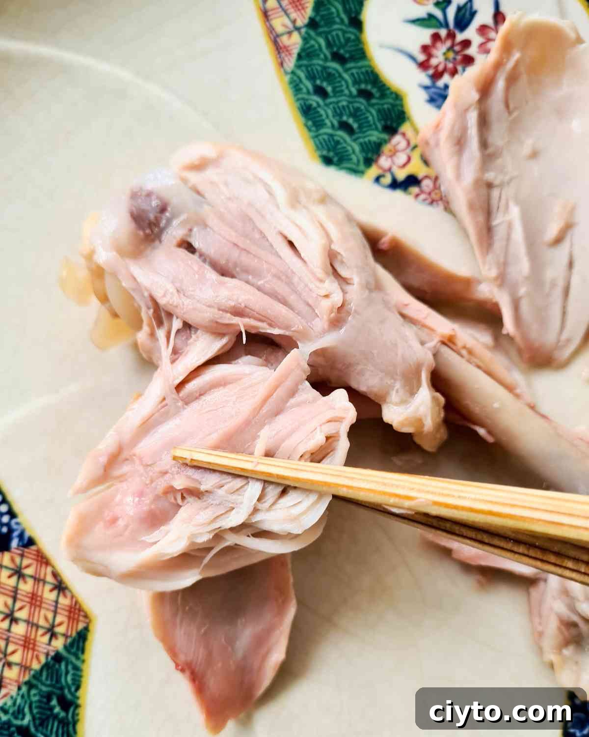 Chicken drumstick with meat being pulled off by a pair of chopsticks