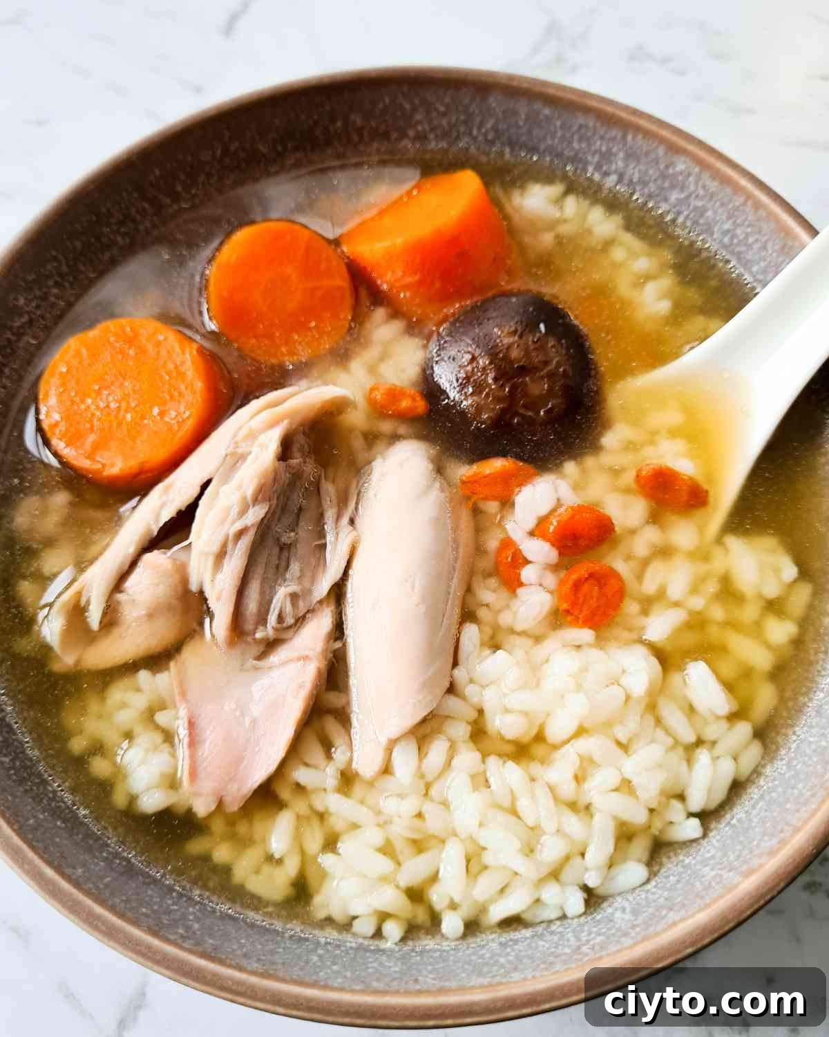 A bowl of clear soup with rice, chicken and carrots
