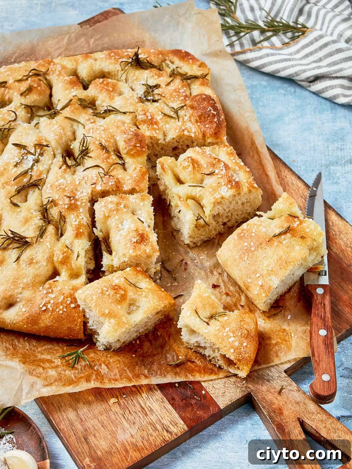Baked focaccia bread sliced into squares, topped with sea salt and rosemary, served on parchment paper.