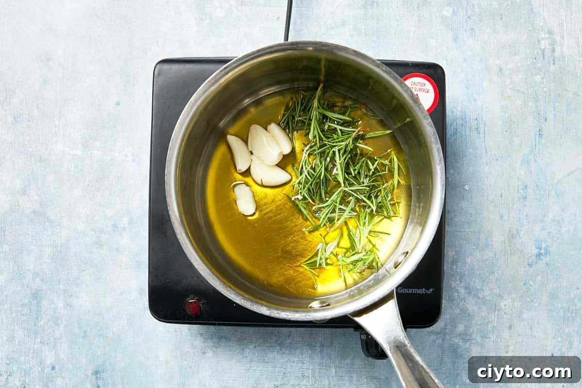 Olive oil infused with rosemary and garlic heating in a small saucepan.
