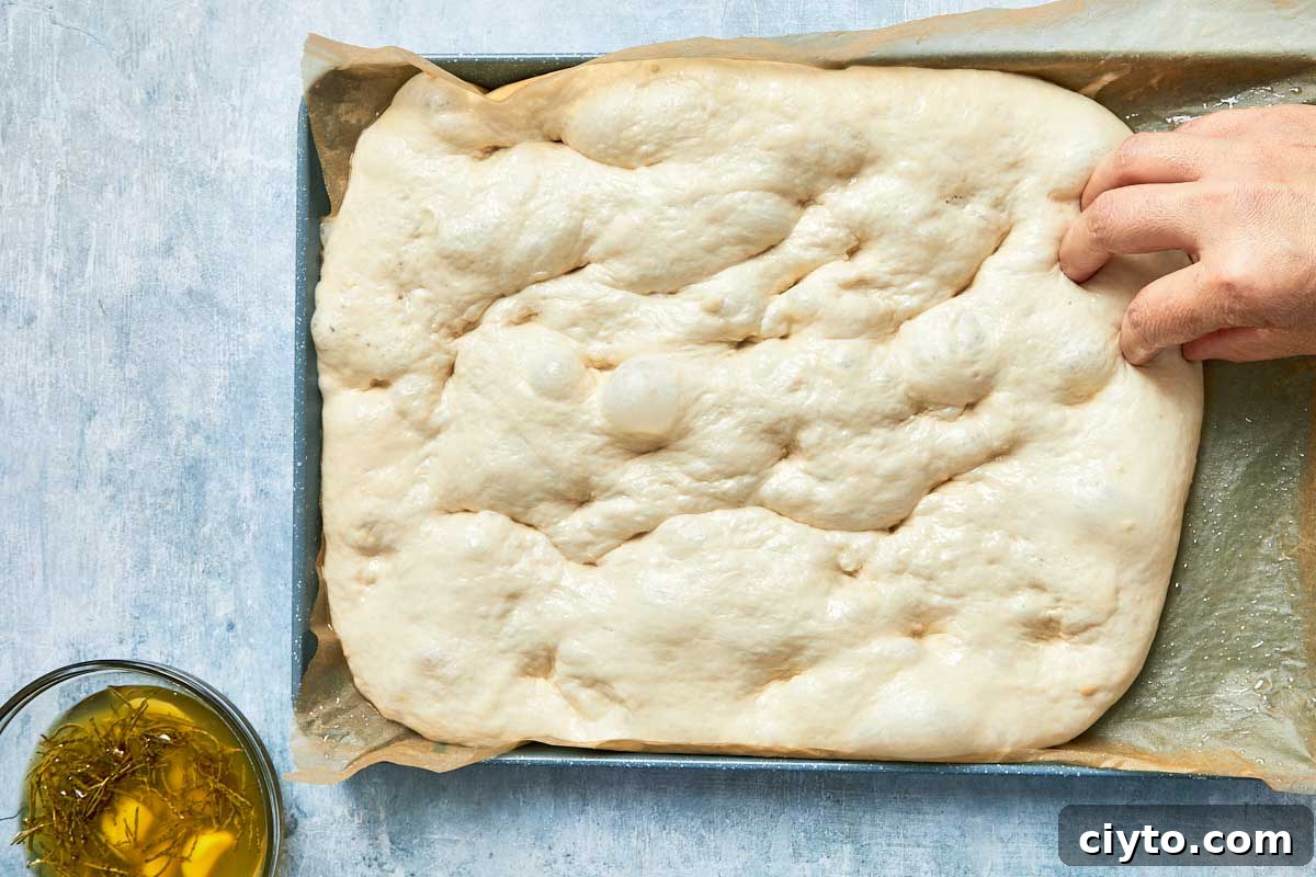Fingers pressing dimples all over the surface of the rested dough.