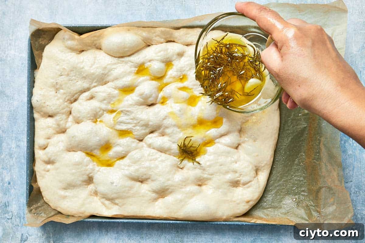 Infused oil being drizzled over dimpled dough before baking.
