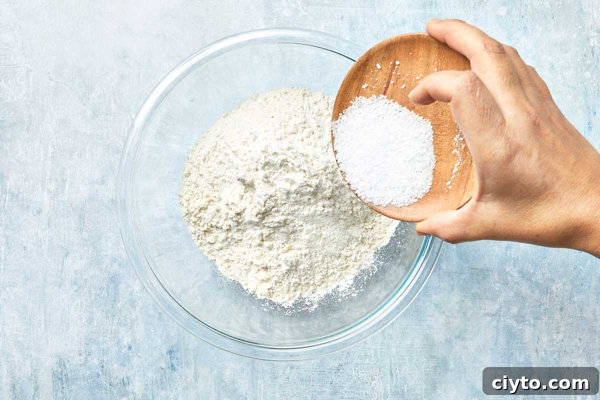 Flour and salt being poured into a large glass bowl.