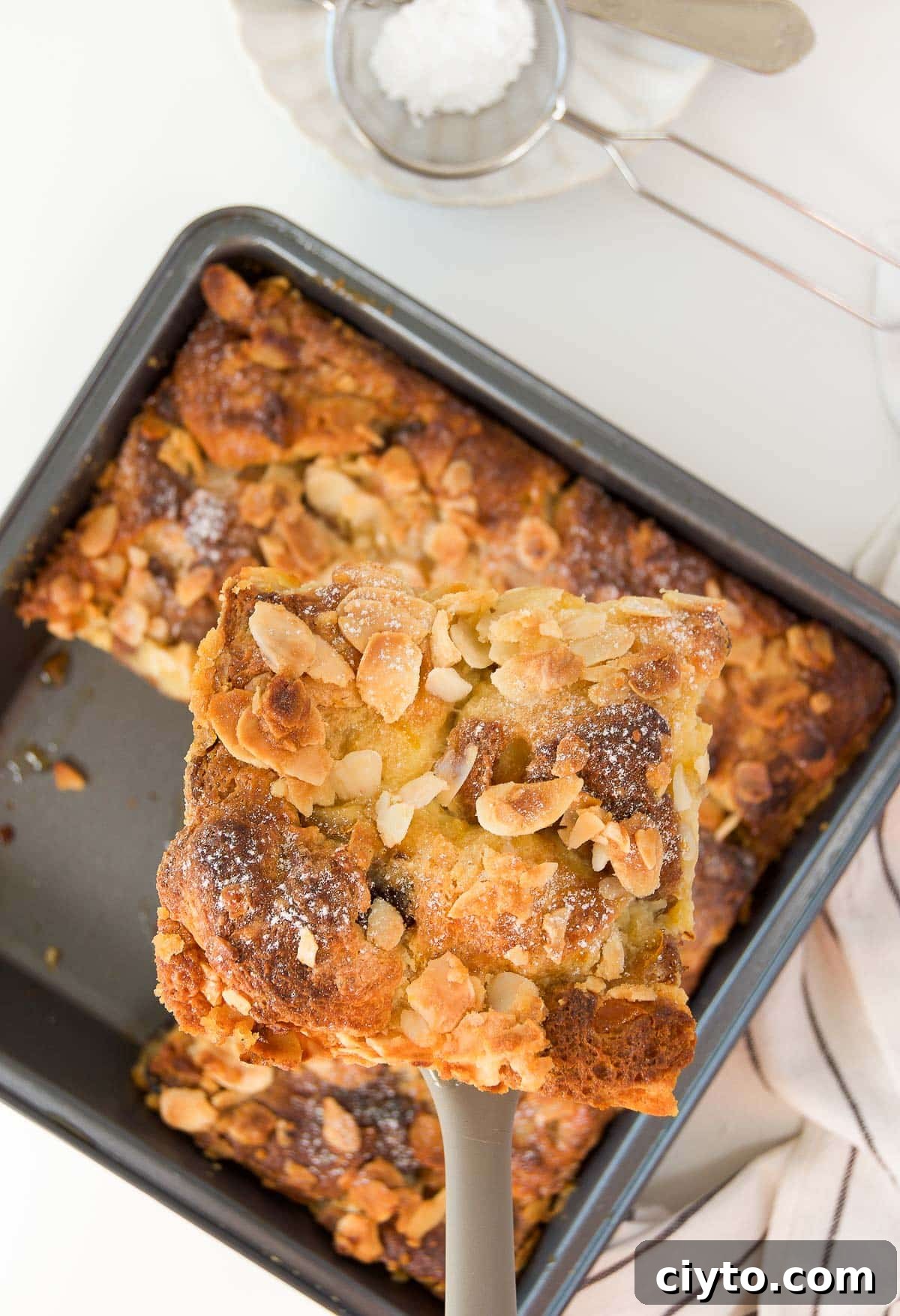 a spatula lifts a slice of panettone bread pudding out of a pan