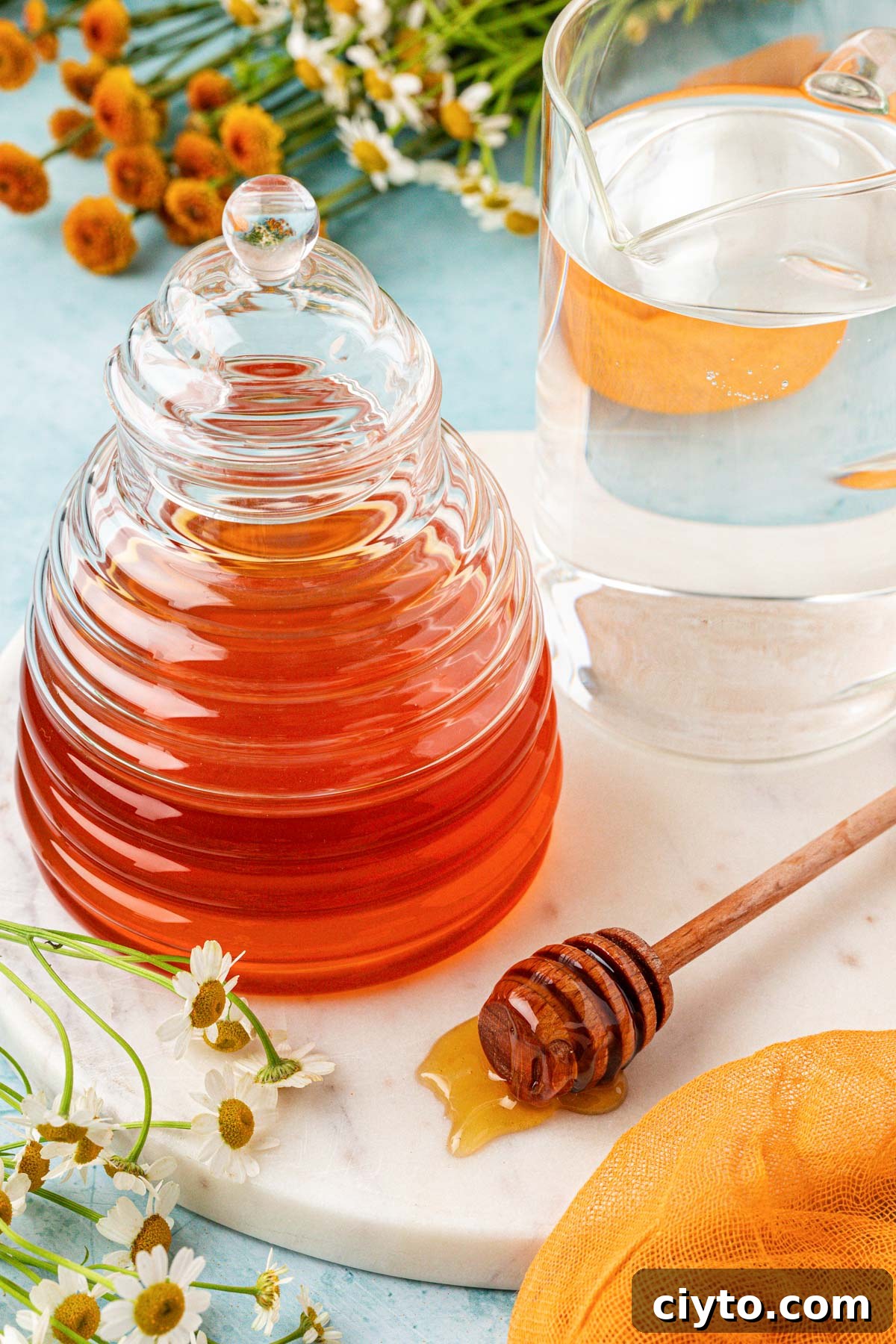 A glass of water and a glass container of honey on a table.