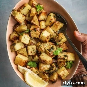 Bowl of spicy and herby potatoes with lemon wedges on the side.