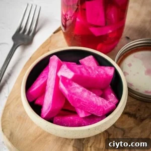 Pink pickled turnips in a bowl on a board.